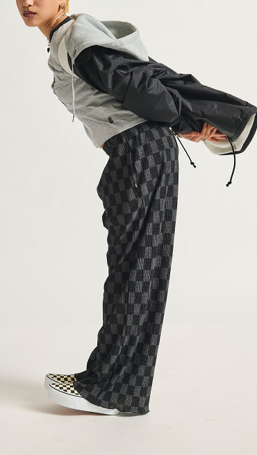 Person in a relaxed pose wearing a gray hoodie, checkerboard pants, and Classic Slip-On Checkerboard Stackform shoes. 
