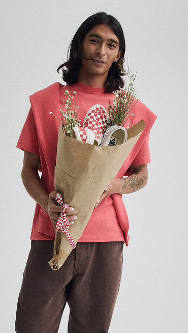 Close-up on a young man holding a bouquet of flowers wearing a pink t-shirt from the Vans Valentine’s Day Collection.