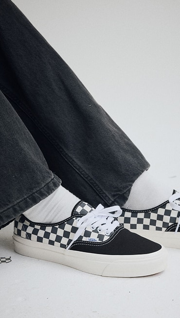 A knee-down shot of someone wearing black and white Checkerboard Premium Authentic with black pants in a photography studio.