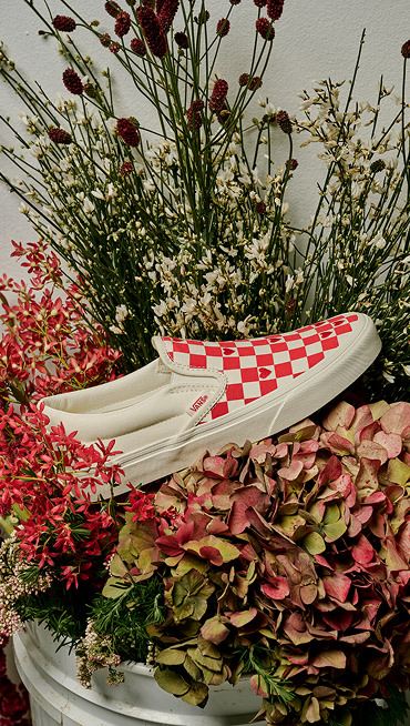 Medium shot of the Classic Slip-On Checkerboard Shoe in Racing Red with hearts in the print resting in the middle of a bouquet.