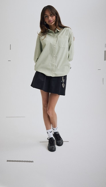 Vans Surf Team Rider Maddie Miller wearing a black Authentic Chino Skirt and a green Utility Shirt in a photography studio.