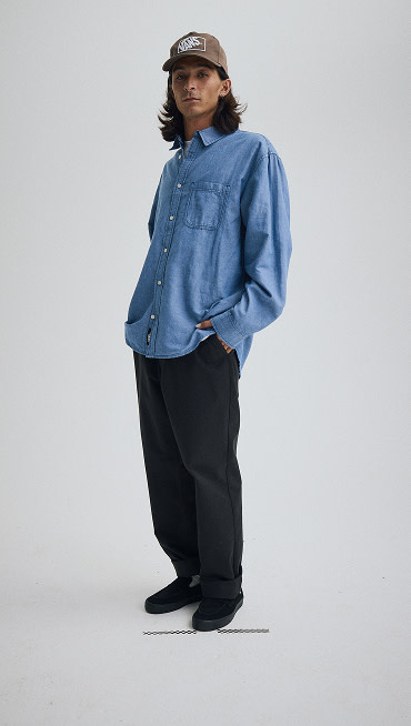 A young man poses in a photography studio wearing black suede Skate Loafers and a denim longsleeve shirt.