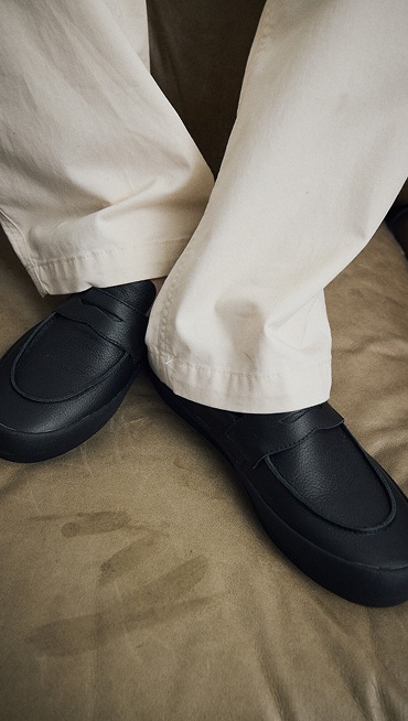Close-up of a man wearing the black Skate Loafer in creme brulee beige OTW by Vans Back Pleated Trousers on a brown carpet.