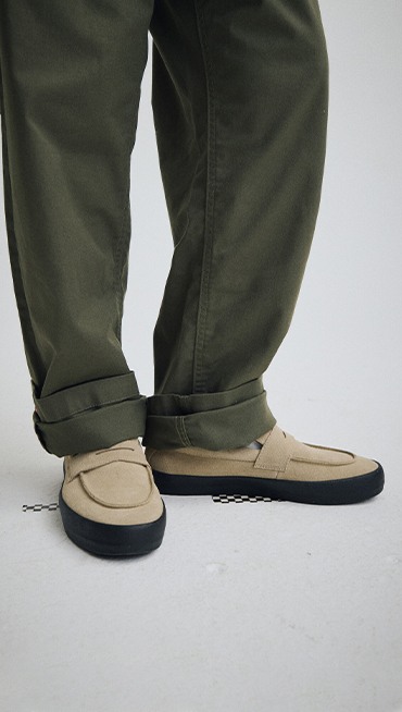 Knee down shot of a person wearing green pants and the Incense Brown / Black Skate Loafer in a grey photography studio.