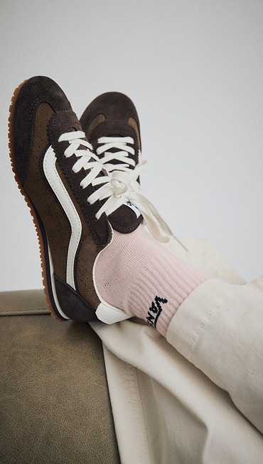 Close-up on someone wearing demitasse brown Super Lowpro with pink Vans crew socks kicked up on the arm of a sofa.