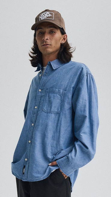 Medium shot of a man looking down at the camera wearing a Vintage Cocoa Brown Vans Formula Snapback Hat and a True Navy Lawson Solid Oxford Shirt.