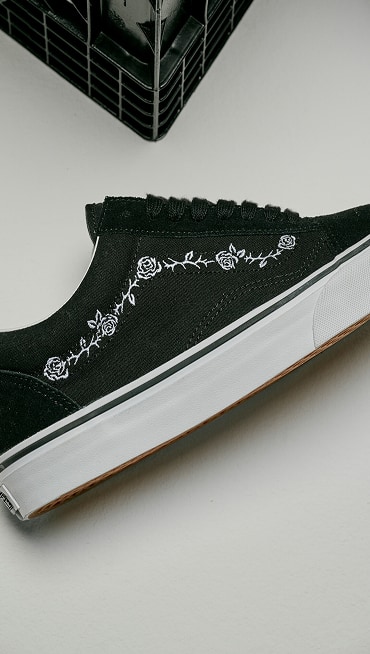 Close up of the Black and White Old Skool Shoe with an embroidered design of thorns and roses laying the floor of a grey photography studio.