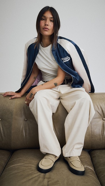 Wide shot of a woman sitting on top of a couch wearing a Dress Blues Souvenir Jacket over her shoulders.