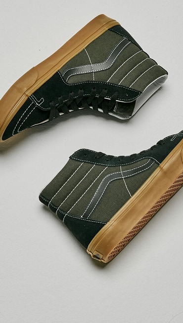 Medium shot of a pair of the Gum Obsidian Fern Green Sk8-Hi laying on the floor of a grey photography studio.