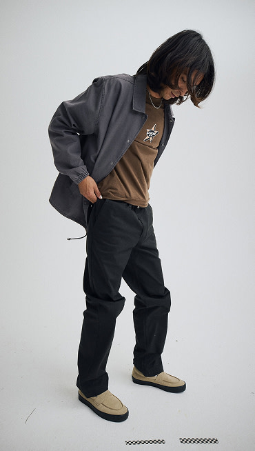 Wide shot of a man wearing an Asphalt Grey Torrey Pigment Canvas Coaches Jacket with a Vintage Cocoa Brown Starmarked T-Shirt.