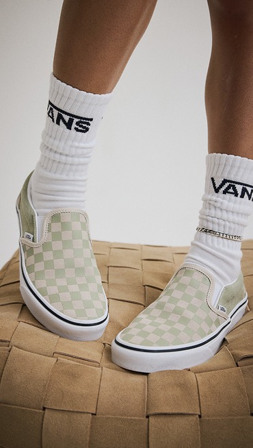 Close-up of someone wearing soft sage green Classic Slip-On Checkerboard Shoe in a photography studio.