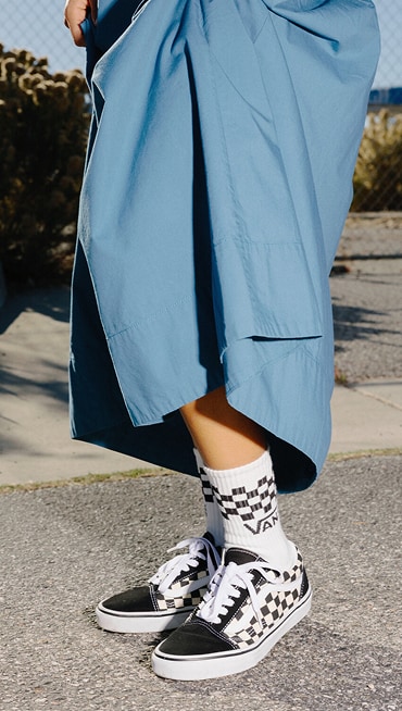 A waist-down shot of someone wearing black and white Old Skool Checkerboard shoes outside on the concrete.