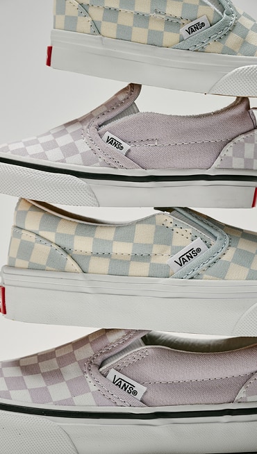 Various kids’ sizes of the Checkerboard Classic Slip-On stacked on top of each other in a photography studio.