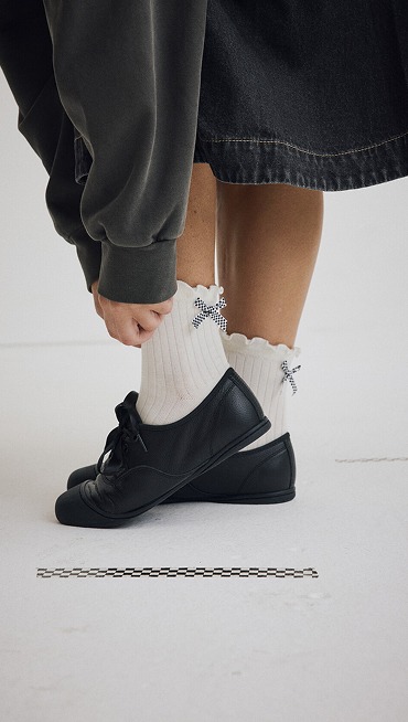 Close-up of a young woman lacing up her black leather Premium Authentic Prima in a photography studio.
