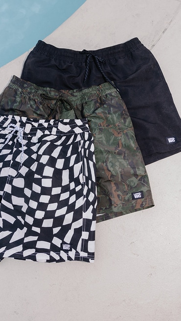 A collection of Vans board shorts laid out on a pool deck beside the water for spring break.