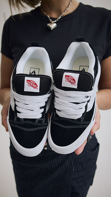 Close-up on a young woman holds up a pair of black and white Knu Skool.
