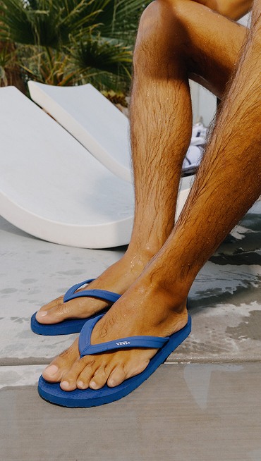 Close-up of a young man wearing light blue Makena Sandals on a pool deck.