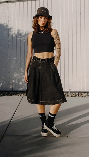 A young woman poses outside wearing a black Authentic Chino Denim Skirt, a black New Salton Tank, and black and white Authentic Platform shoes.
