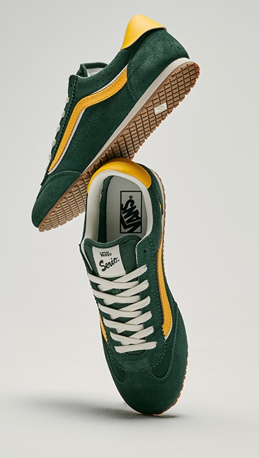 A pair of green and yellow Super Lowpro shoes floating in the air in a photography studio.