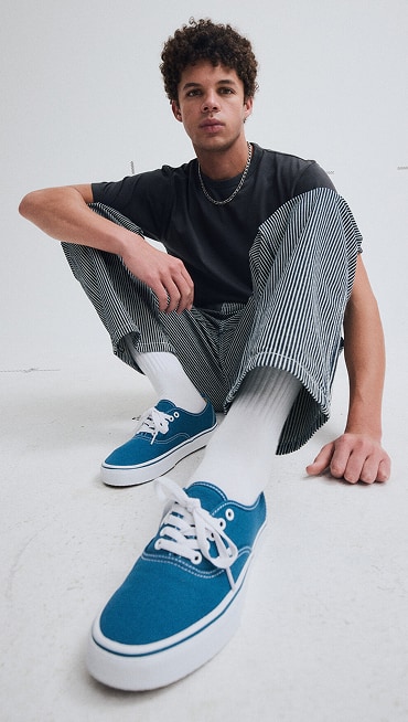 A fisheye shot of a young man sitting on the floor of a photography studio wearing blue Authentic shoes.