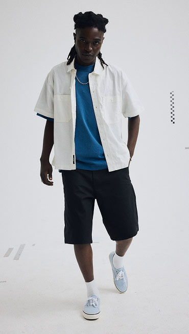A young man wearing light blue Authentic, a white Larkspur Solid Shirt, and black Authentic Chino Baggy Shorts in a photography studio.
