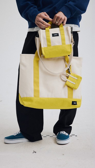 Waist down medium shot of someone holding three different sizes of yellow and white Pergs totes and bags.