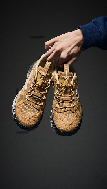 Medium shot of a person holding a pair of the Crosspath XC in Autumn Brown with a black studio background.