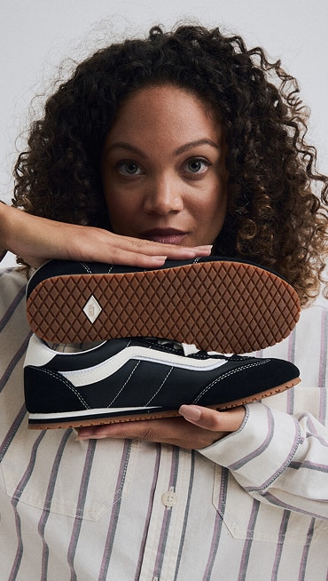 Close-up on a young woman holding a pair of black and white Super Lowpro while looking into the camera in a photo studio.