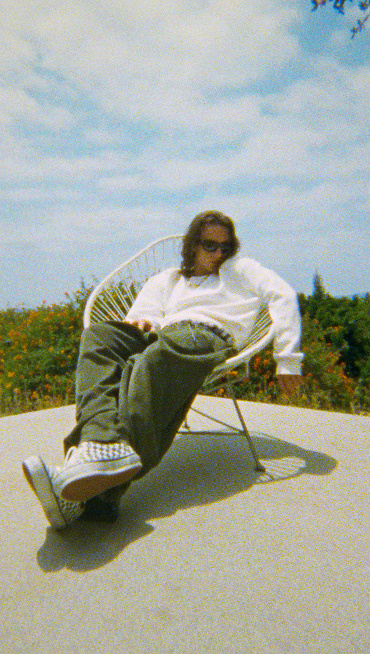 A man sitting in a chair outside wearing OTW Era 95 DST checkerboard shoes