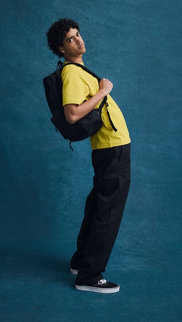 A young man poses against a picture day backdrop in Vans shoes, clothes, and a backpack for Back to School.