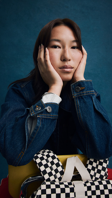 Close-up on a young woman posing for Back to School with a Checkerboard Scatter Backpack and a dark blue Emily Boxy Work Wear Jacket.
