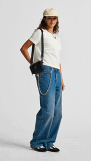 A girl poses with Block Wallet Checkerboard Bag and Sirelle 5 Pocket Puddle Pants in a photography studio.