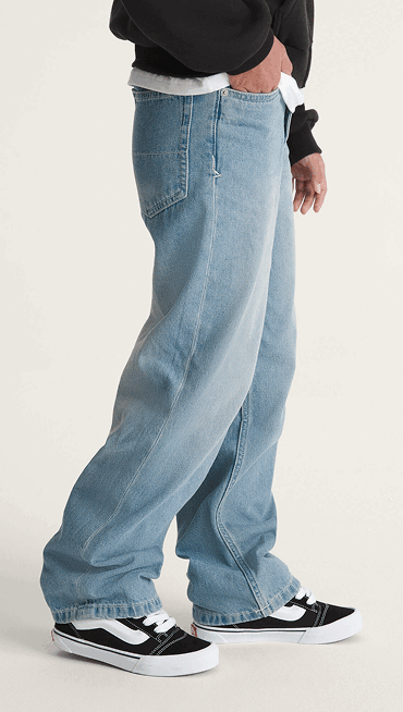 A waist-down shot of a kid wearing black and white Knu Skool with blue jeans.