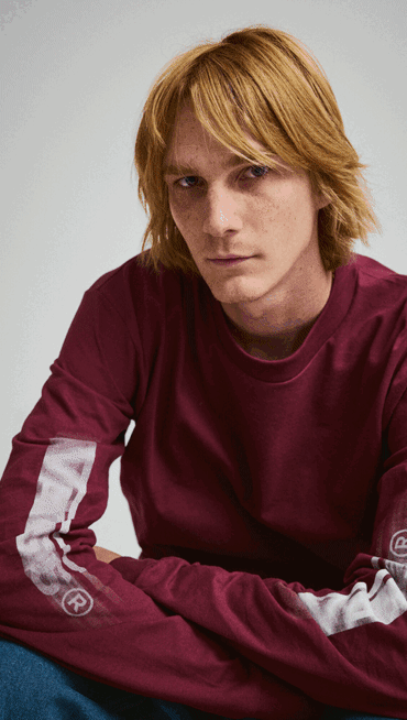 A young man looks into the camera wearing a red Blur Drop Long Sleeve T-Shirt.