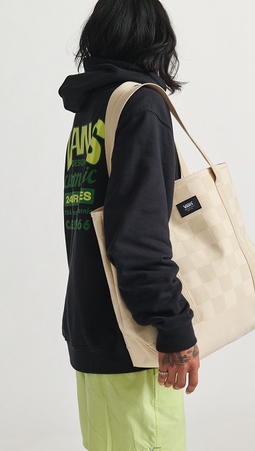 A person looking away from the camera with a beige Checkerboard bag wearing a black hoodie.