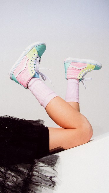 A girl lays on the ground with her Sk8-Hi hanging in the air.