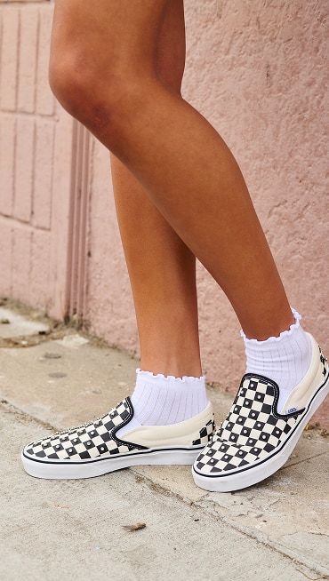 A close-up of a girl wearing rhinestone-embedded black and white Checkerboard Classic Slip-On.