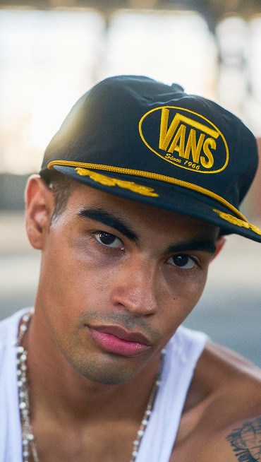 Portrait of a man posing in a black Scrambled Vans Snapback Hat, styled with a white tank top.