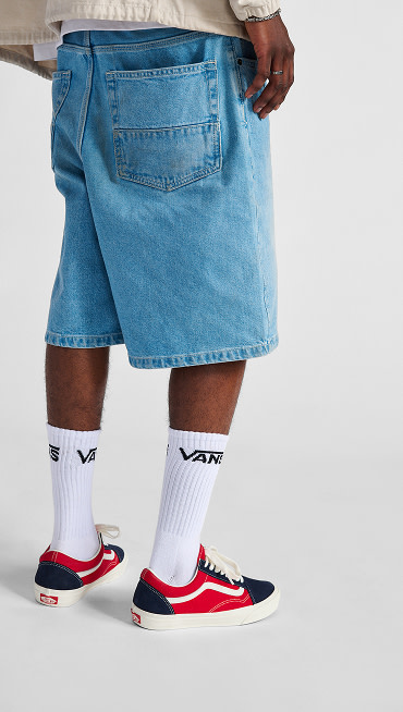 Waist down studio shot of a man wearing denim shorts, white Vans socks and Vans Old Skool shoe in Navy Blue/Red.