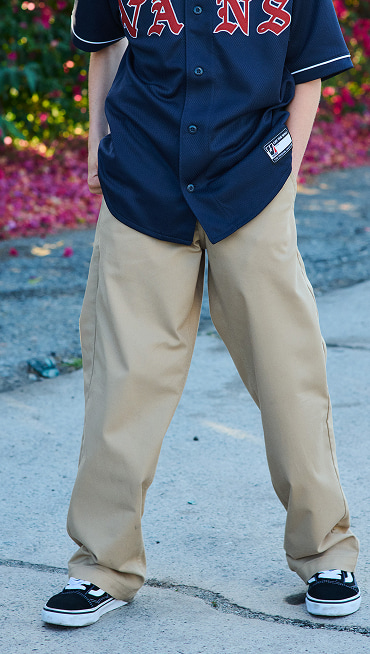 A chest-down shot of a boy wearing a Vans baseball shirt, brown chinos, and black and white Old Skool.