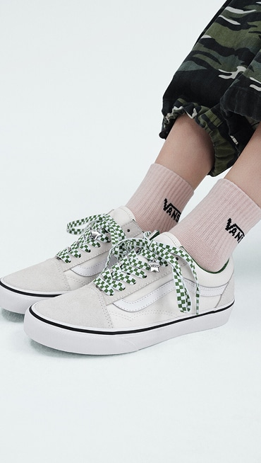 A pair of beige Old Skool styled with green Checkerboard laces and Vans shoe charms.