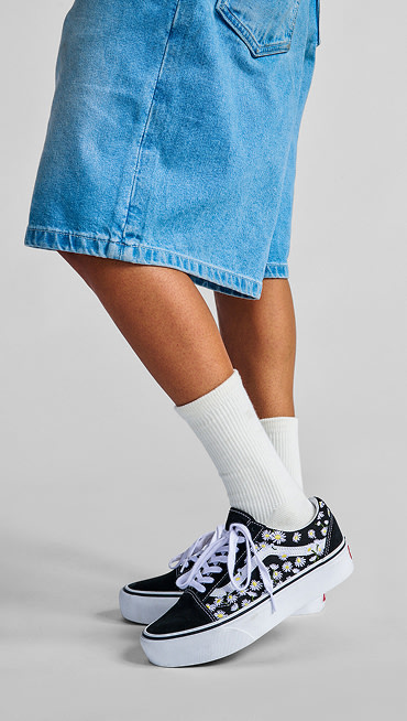 A waist-down shot of a man wearing Premium Jorts, white crew socks, and navy blue and red Old Skool.
