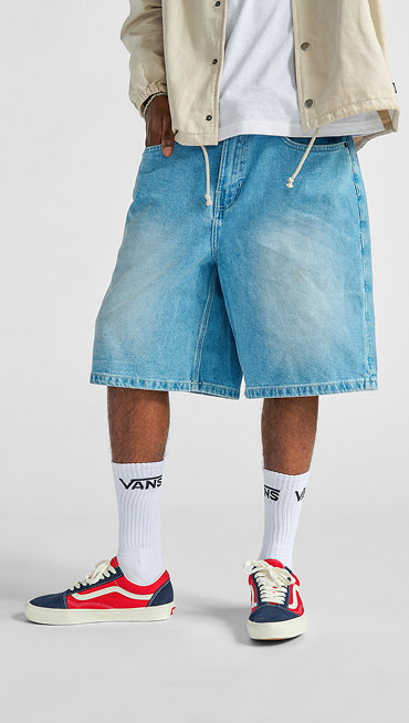 A waist-down shot of a man wearing Premium Jorts, white crew socks, and navy blue and red Old Skool.