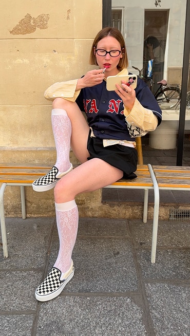 Influencer @volgaleoni does her makeup outside of a coffee shop wearing knee-high socks and black and white Checkerboard Classic Slip-On.