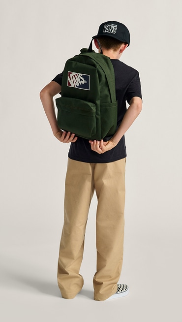 A boy adjusts the dried kelp green Kids Old Skool Grom Backpack in a photography studio.