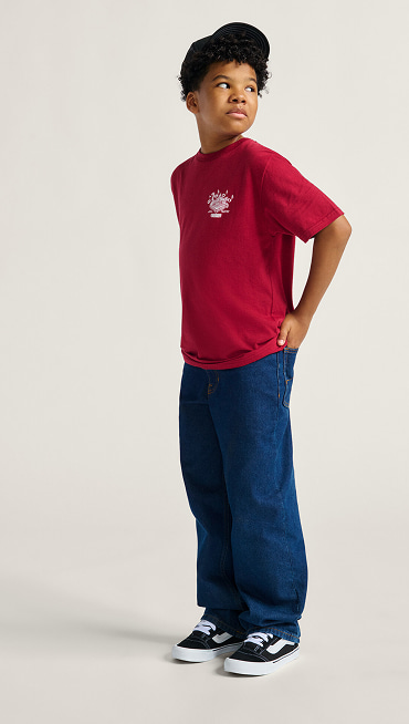 A young boy looks over his shoulder in a photography studio wearing black and white Knu Skool, blue jeans, and a red t-shirt.