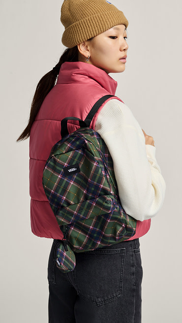A woman poses in a photography studio wearing a mauvewood MTE Hillgate Cropped Vest and a pine forest Old Skool Mini Backpack.