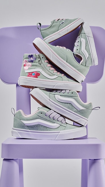 A stack of gray and olive green kids’ shoes including Authentic, Knu Skool, and Sk8-Hi.