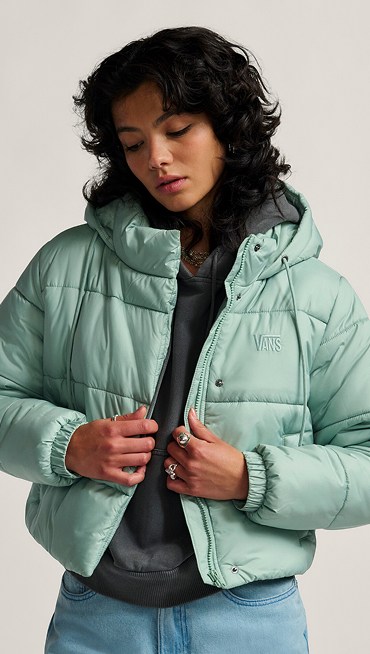 A waist-up shot of a young woman posing in an asphalt gray Retro PO Hoodie and a light blue MTE Hillgate Cropped Puffer in a photography studio.