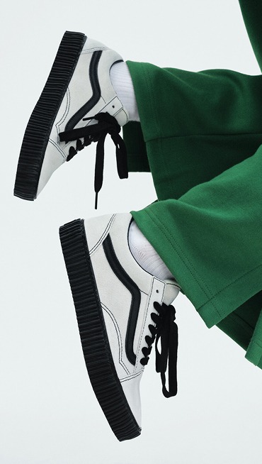 A close-up of someone jumping wearing black and white Old Skool styled with green pants.